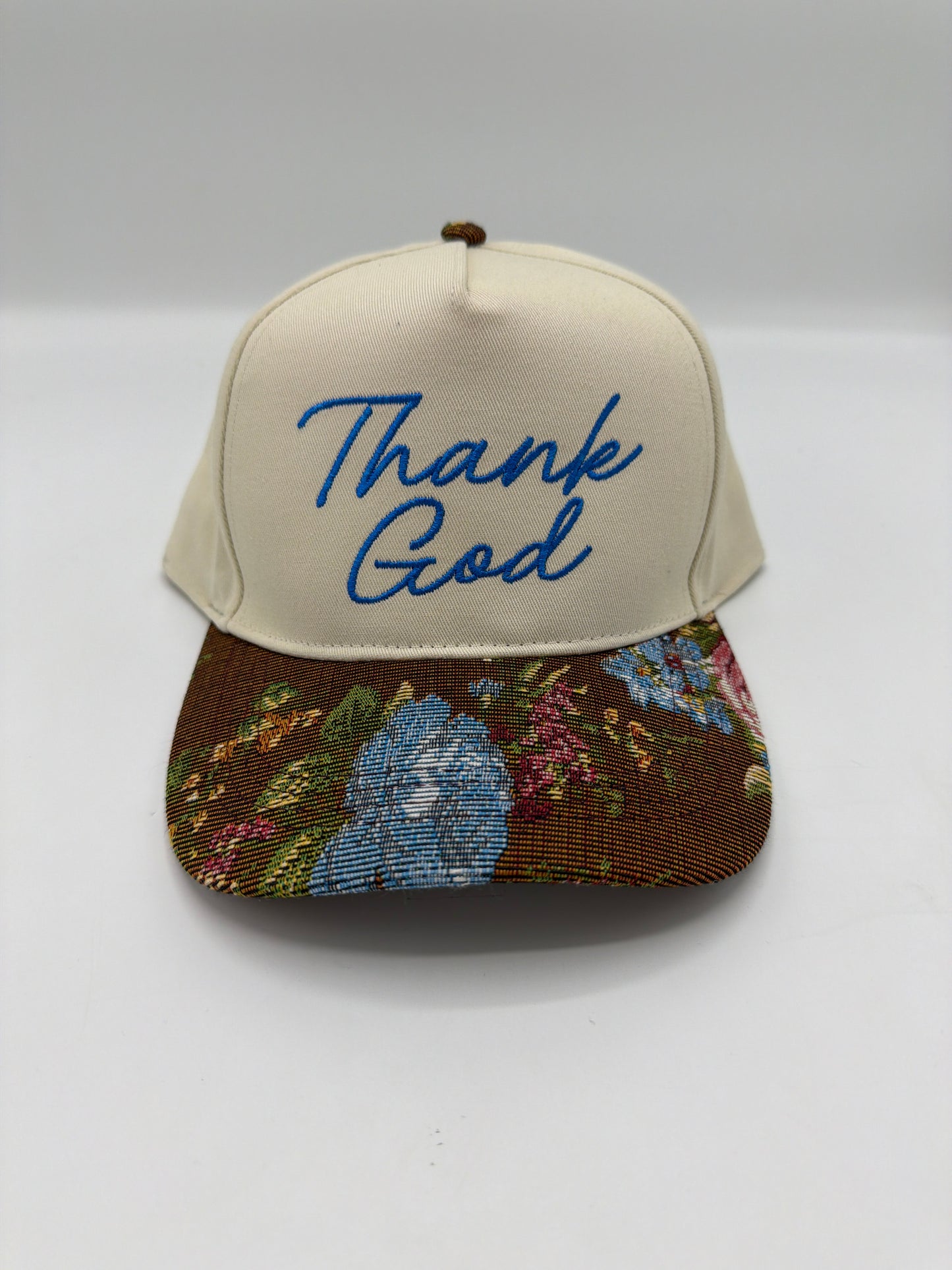 Thank God in royal blue script on a cream crown with a brown floral tapestry brim