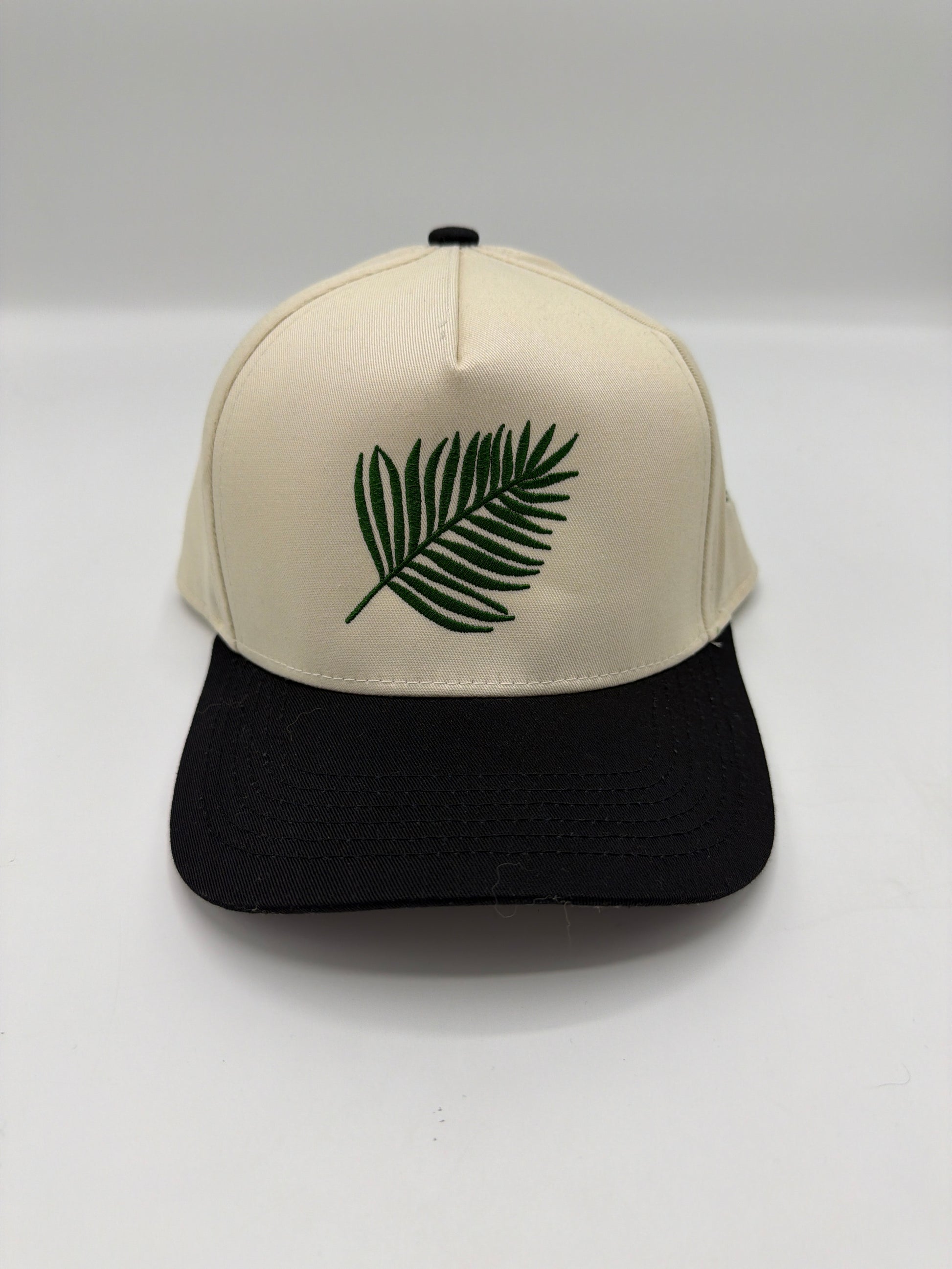 Embroidered palm leaf on the front panel of a cream five panel snapback with a black brim