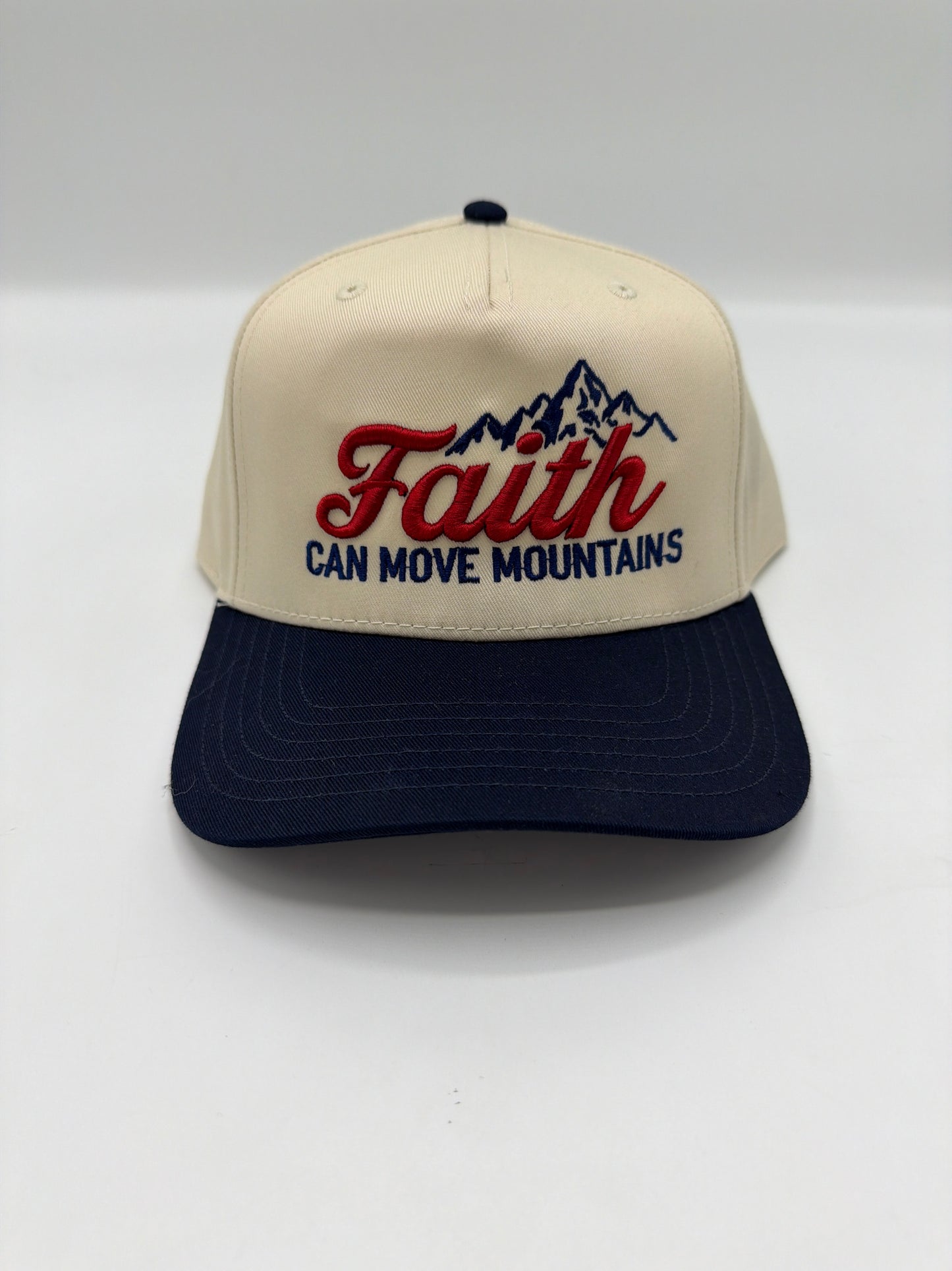 Faith Can Move Mountains with an embroidered mountain range on a cream crown with a navy brim