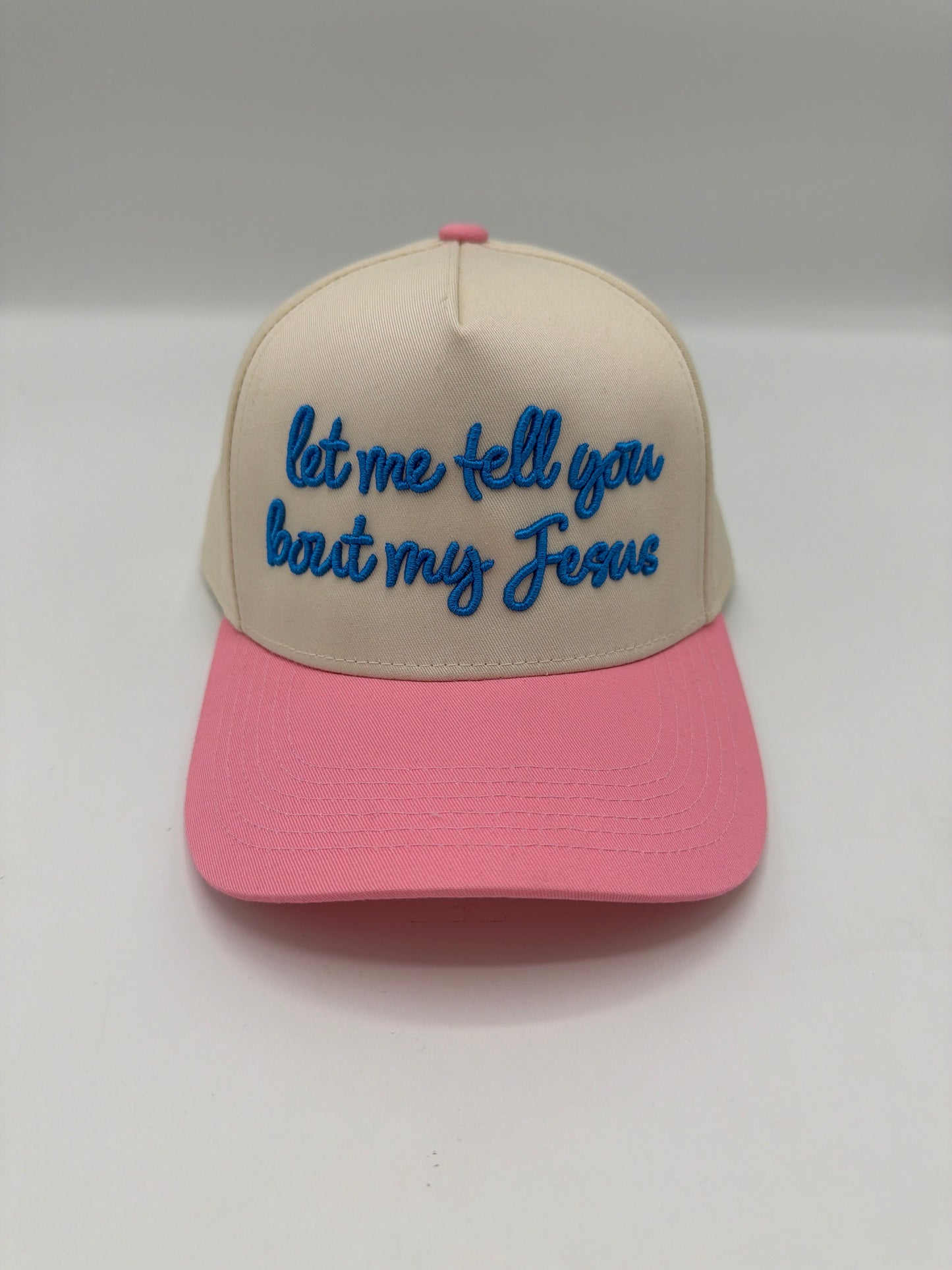 Let me tell you bout my Jesus in blue script on a cream crown with a pink brim